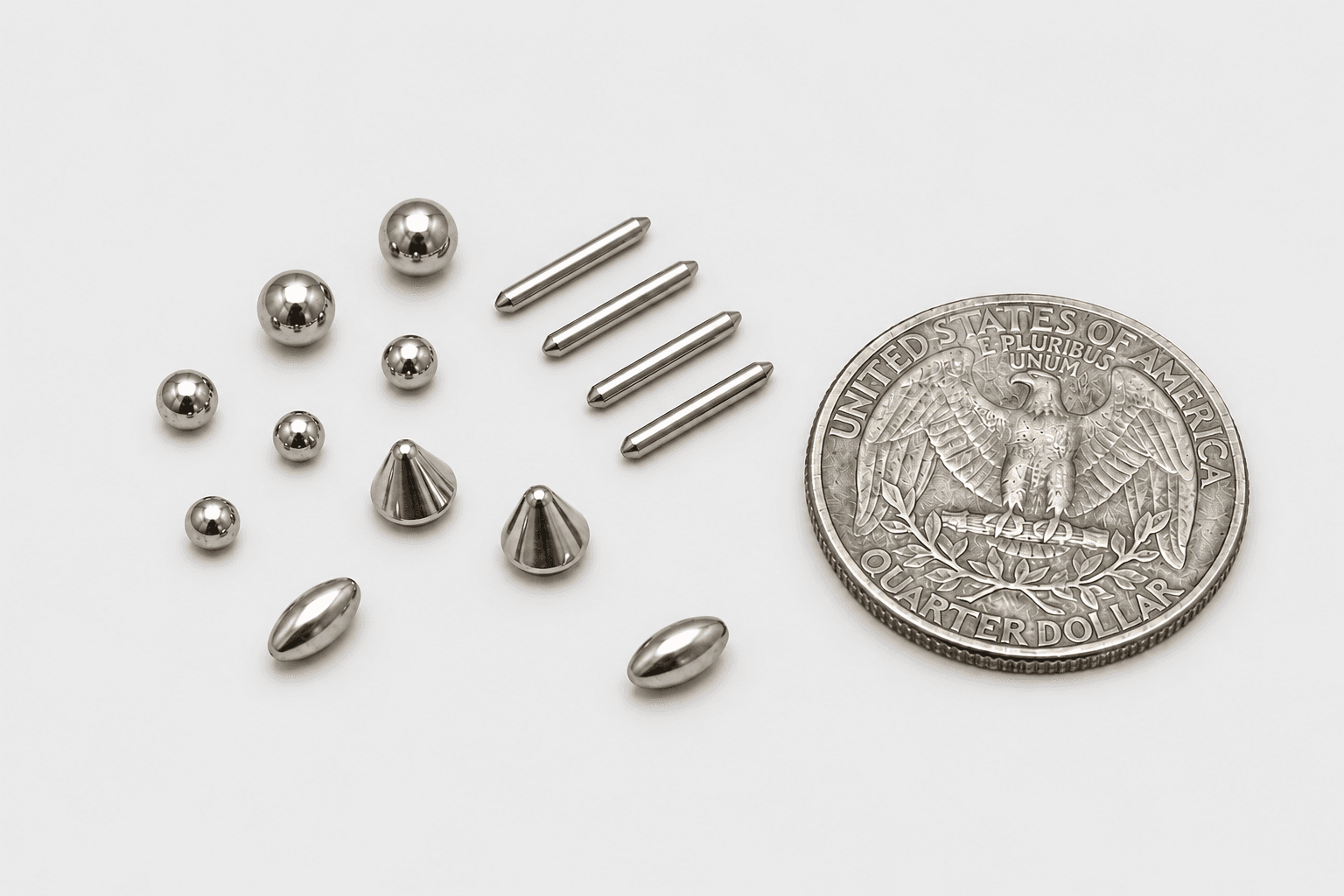 Polished metal balls, pins, and cone shaped pieces arranged beside a US quarter