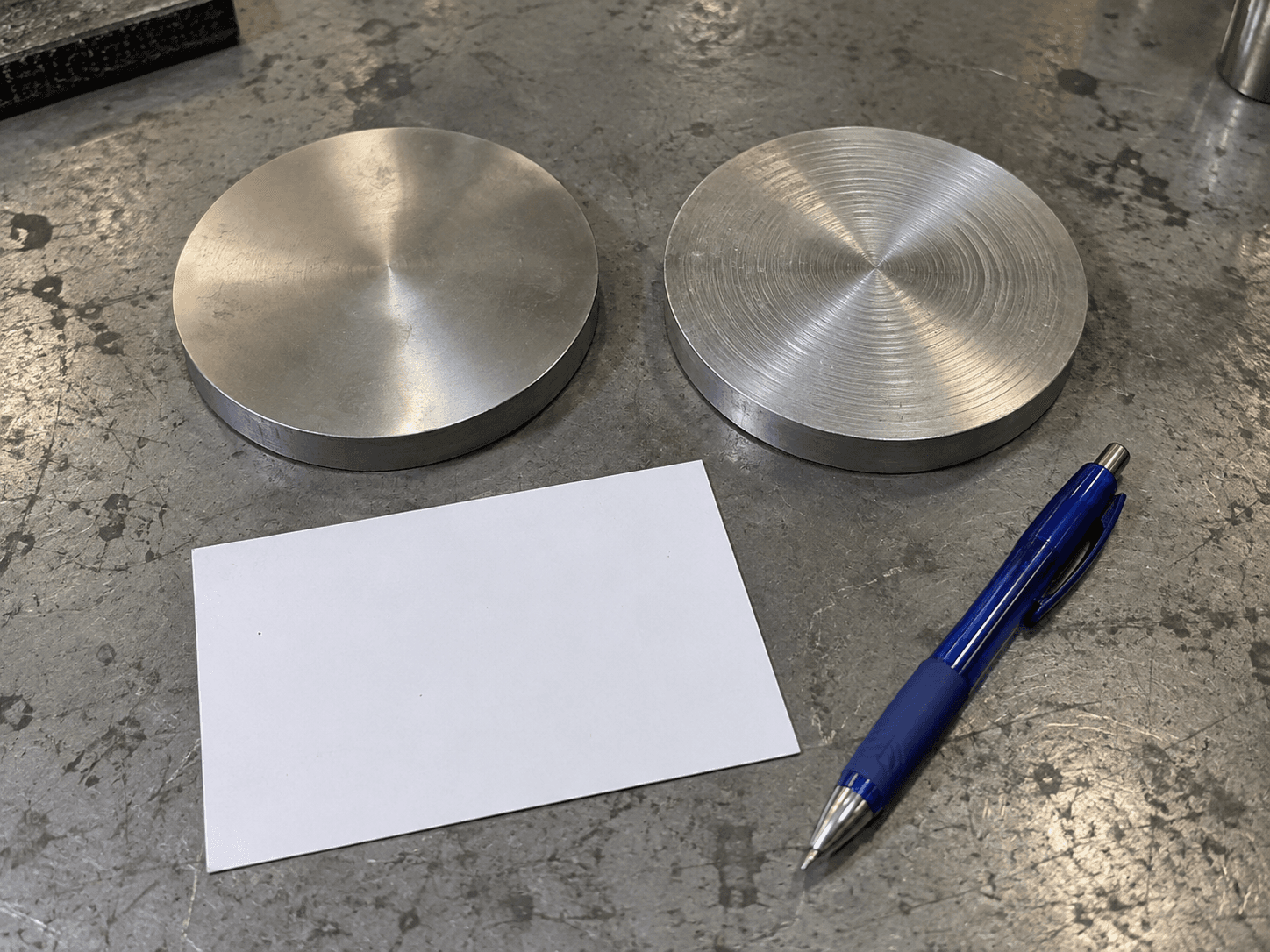 AI illustration of two generic metal discs, a blank card and a blue pen on a scuffed workshop bench.