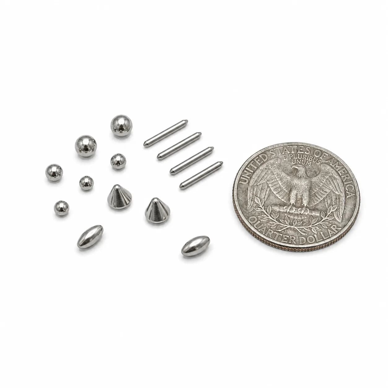Polished metal balls, pins, and cone shaped pieces arranged beside a US quarter